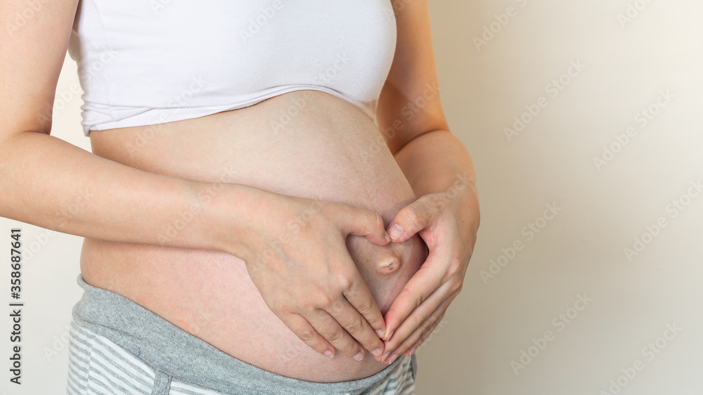 The hands of the pregnant woman that heart shaped symbol put on a belly. Concept of pregnancy The hands of the pregnant woman that heart shaped symbol put on a belly. Concept of pregnancy