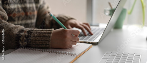 Female university student online learning with laptop and stationery on worktable at home
