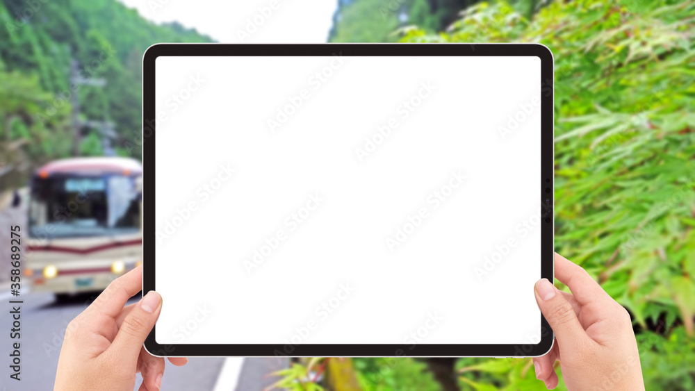 Two hands holding white screen mockup tablet computer, bus and road in Japan countryside .