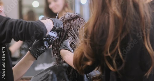 women apply hair bleach on beauty salon visitor head with special black brushes slow motion close view