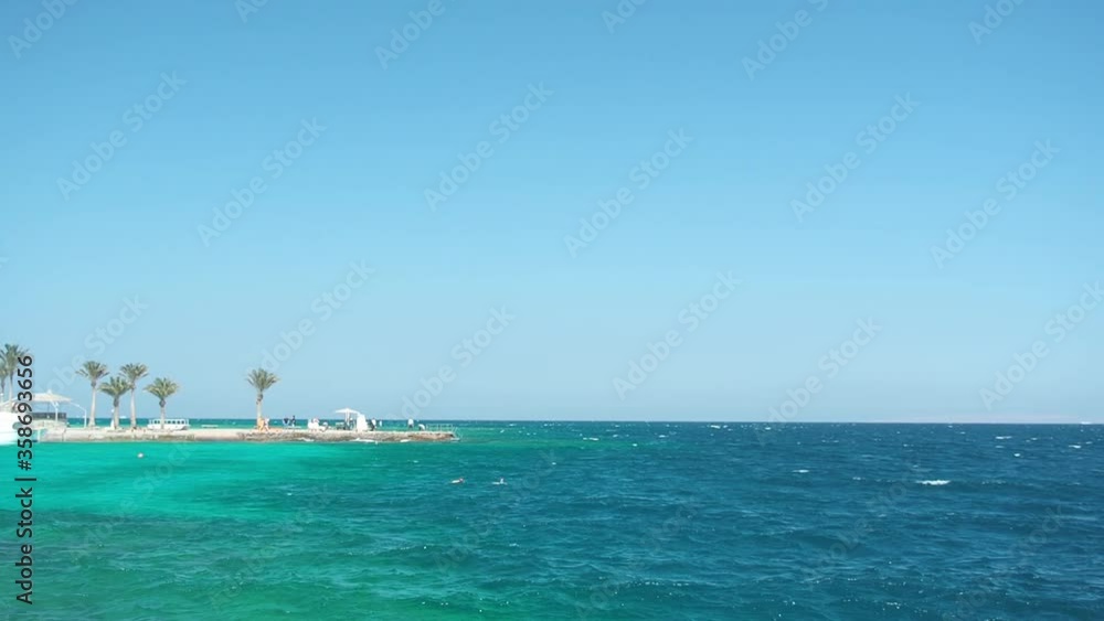Seascape of egyptian coastline, extreme wide shot. Tourists snorkeling on surface. Green palms under clear blue sky. Photographed in Hurghada in february. Selective soft focus. Blurred background Seascape of egyptian coastline, extreme wide shot. Tourists snorkeling on surface. Green palms under clear blue sky. Photographed in Hurghada in february. Selective soft focus. Blurred background