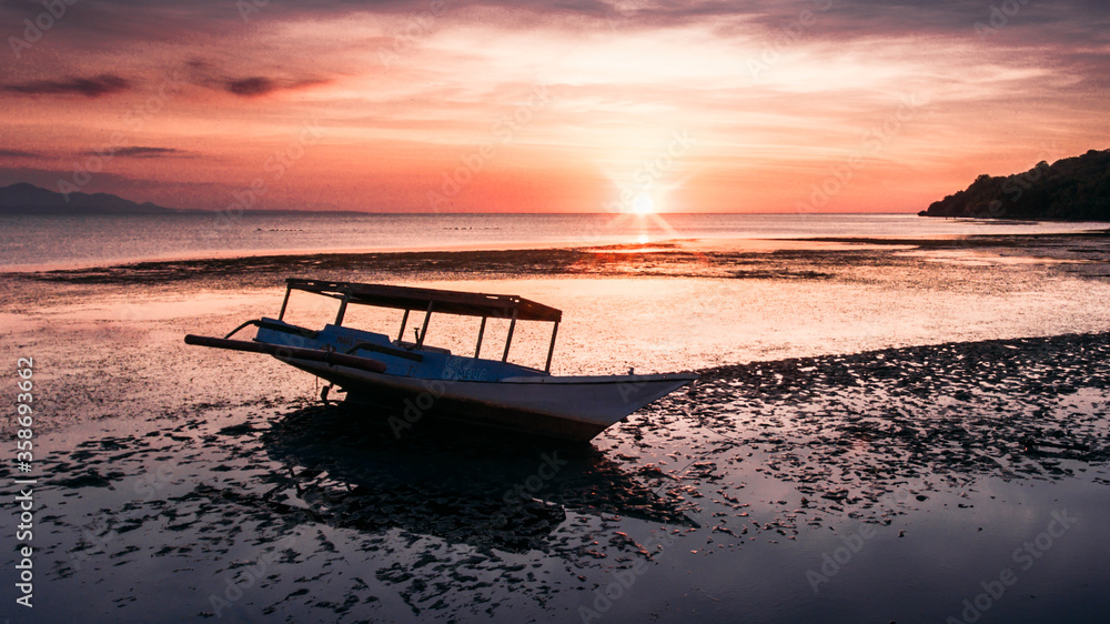 Beautiful beach with wooden boat and low tide water at sunset time in Ai Lemak Beach, Sumbawa, Indonesia