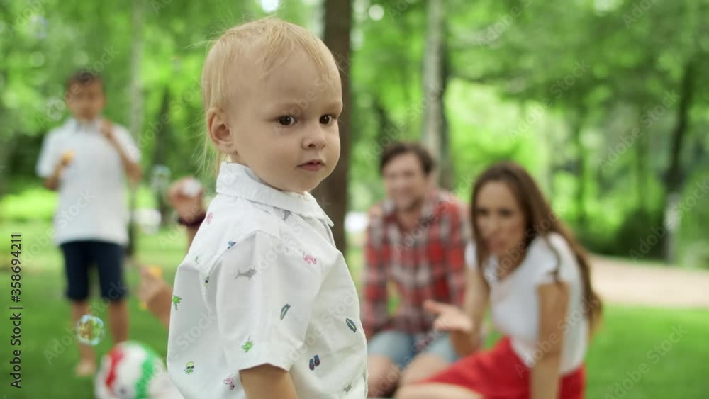 Toddler looking at camera with family. Children blowing soap bubbles in forest Toddler looking at camera with family. Children blowing soap bubbles in forest