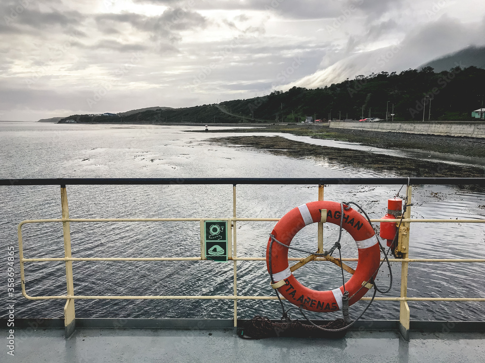 Puerto Williams coast, sea, mountains and beach from a ferry boat with a lifebuoy, in a cloudy day, Chile