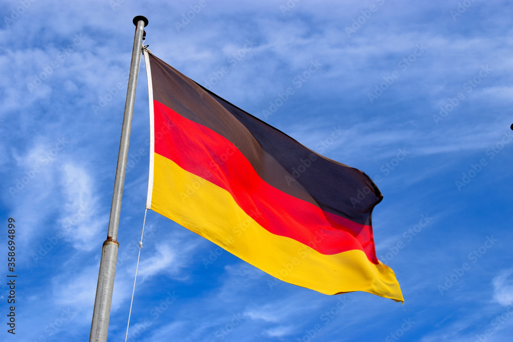 German flag dancing in the wind on a flag pole with the blue sky in the background. German flag dancing in the wind on a flag pole with the blue sky in the background.
