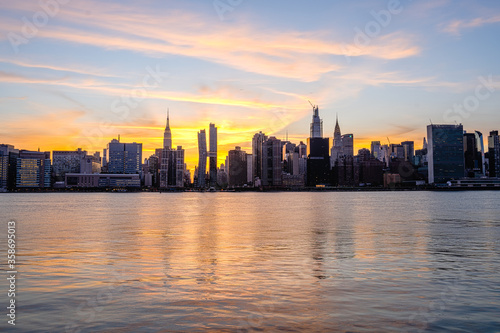 Manhattan Midtown skyline wide angle view on Empire State building, Chrysler building, American Copper Buildings, Headquarters of the United Nations. Sunset, orange sky, reflections in water © valeragf