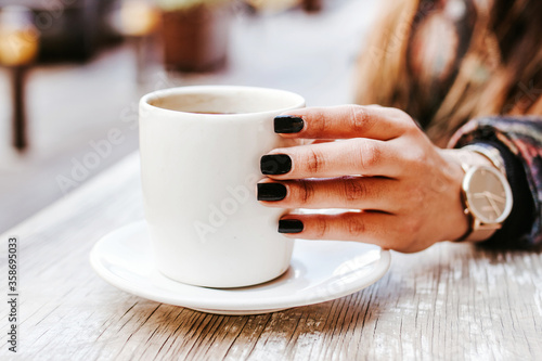 woman hand holding a cup of coffee outdoors at coffee shop or cafe with blurred background