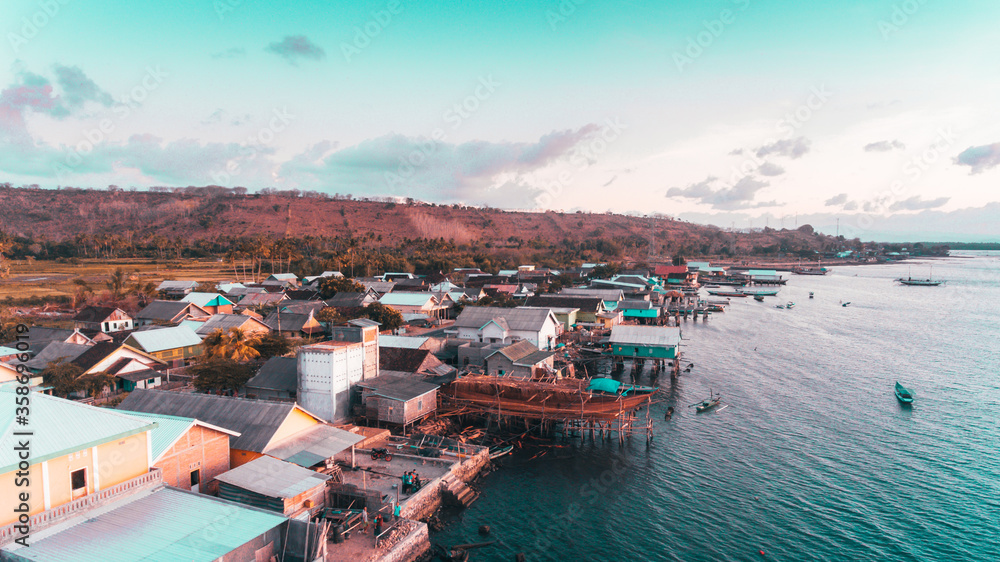 Aerial view of fisherman village in Labuan Jambu, Sumbawa, Indonesia. Traditional house with wooden pier on sea water with blue sky