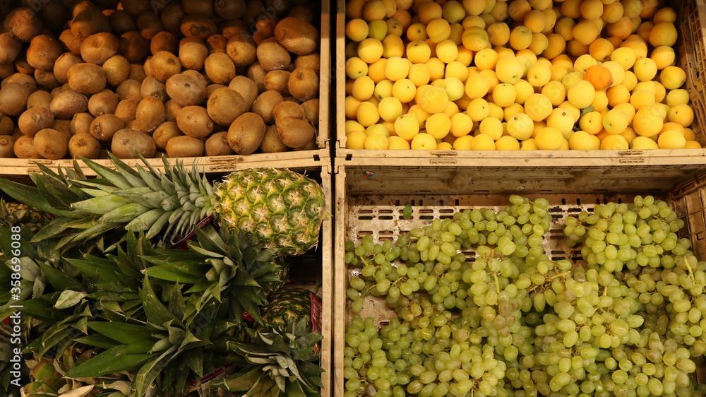 kiwi, pineapple, apricots and grapes in wooden boxes in an open display case in a self-service store