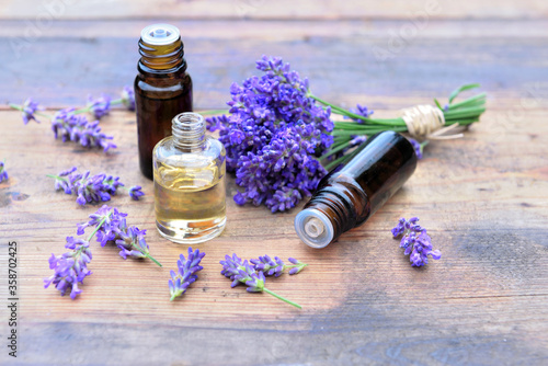 bottles of essential oil and bouquet of lavender flowers arranged on a wooden table