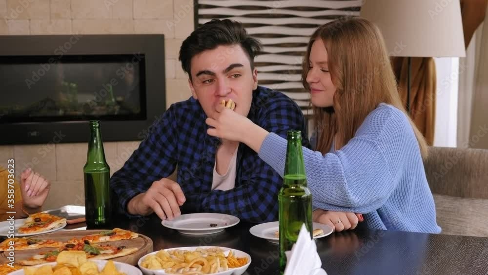 A couple in love is relaxing with friends in a pizzeria, the girl feeds the guy pizza. Friends drink beer and eat pizza in the cafe in the evening. Slow motion. A couple in love is relaxing with friends in a pizzeria, the girl feeds the guy pizza. Friends drink beer and eat pizza in the cafe in the evening. Slow motion.