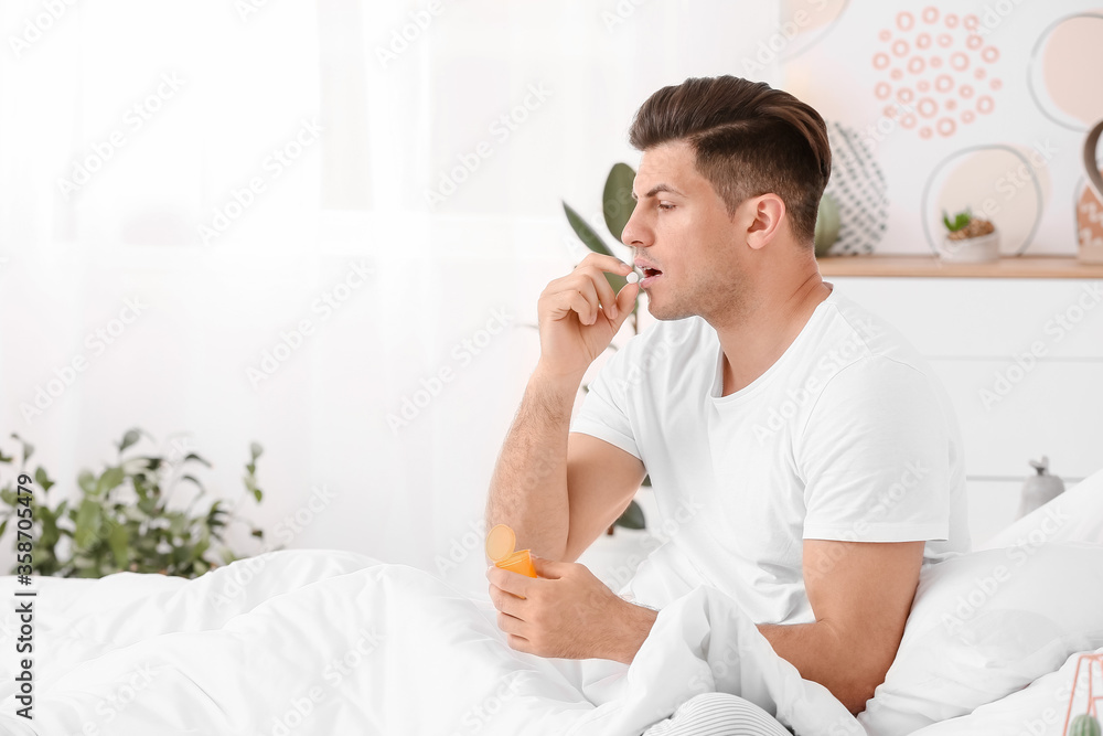 Young man taking sleeping pills in bedroom Young man taking sleeping pills in bedroom