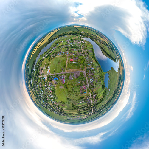 Aleksandrovsky farm in the south of Russia, surrounded by fields near a flat river with a dam - little planet aerial panorama with a sunny and rainy day