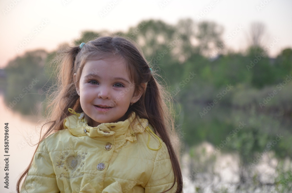 a little girl in an autumn or spring jacket stands near the lake, smiles. A tourist by a small lake with a deep blue bottom. The nature a little girl in an autumn or spring jacket stands near the lake, smiles. A tourist by a small lake with a deep blue bottom. The nature
