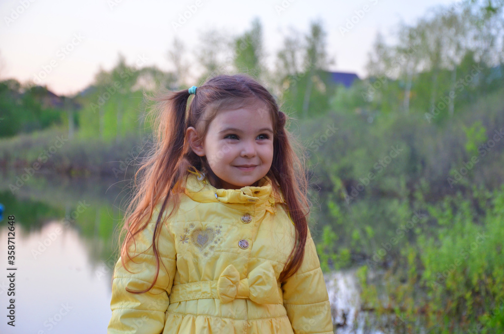 a little girl in an autumn or spring jacket stands near the lake, smiles. A tourist by a small lake with a deep blue bottom. The nature a little girl in an autumn or spring jacket stands near the lake, smiles. A tourist by a small lake with a deep blue bottom. The nature