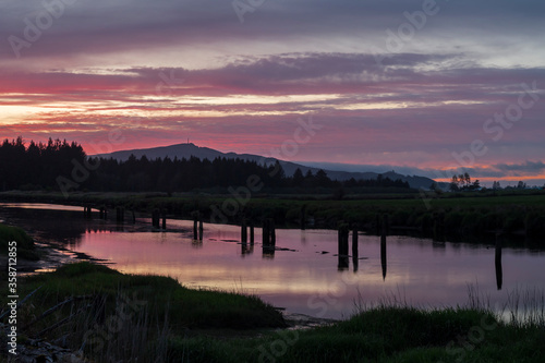View of vibrant colors sunset landscape. Silhouetted hills and plants reflect in calm water of the river. Location is Tillamook river in Oregon, USA © Victoria