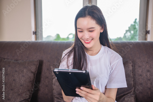 Asian young woman is playing a digital tablet computer and sitting on the sofa at home © tuiphotoengineer
