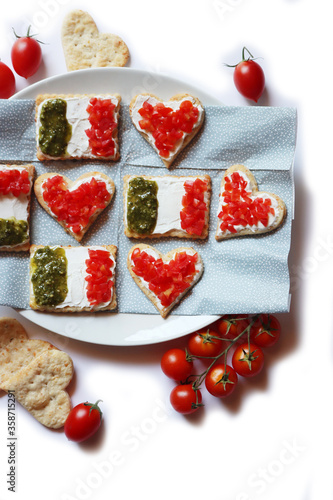 Salty cookies in shape of red heart and italian flag on a plate isolated on white. Snack with tradional italian ingredient: pesto, cheese and red tomatoes.
