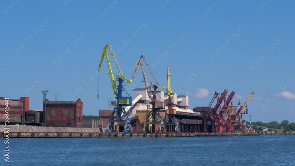 Port cranes and harbor warehouses in sunny calm summer day at Port of Ventspils, wide shot from a distance Port cranes and harbor warehouses in sunny calm summer day at Port of Ventspils, wide shot from a distance