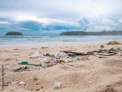 Environmental pollution. Ecological problem. Garbages, plastic, and wastes on the sandy beach of tropical sea. Island and mountain background.