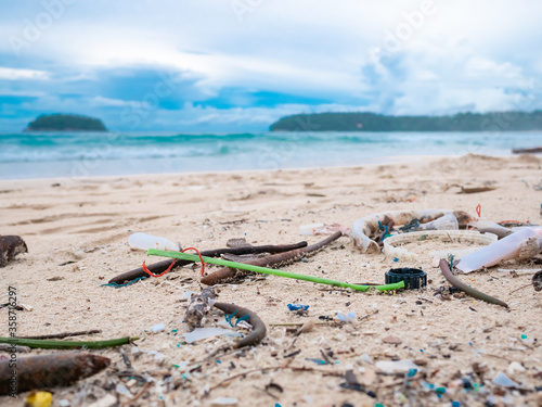 Environmental pollution. Ecological problem. Garbages, plastic, and wastes on the sandy beach of tropical sea. Island and mountain background.