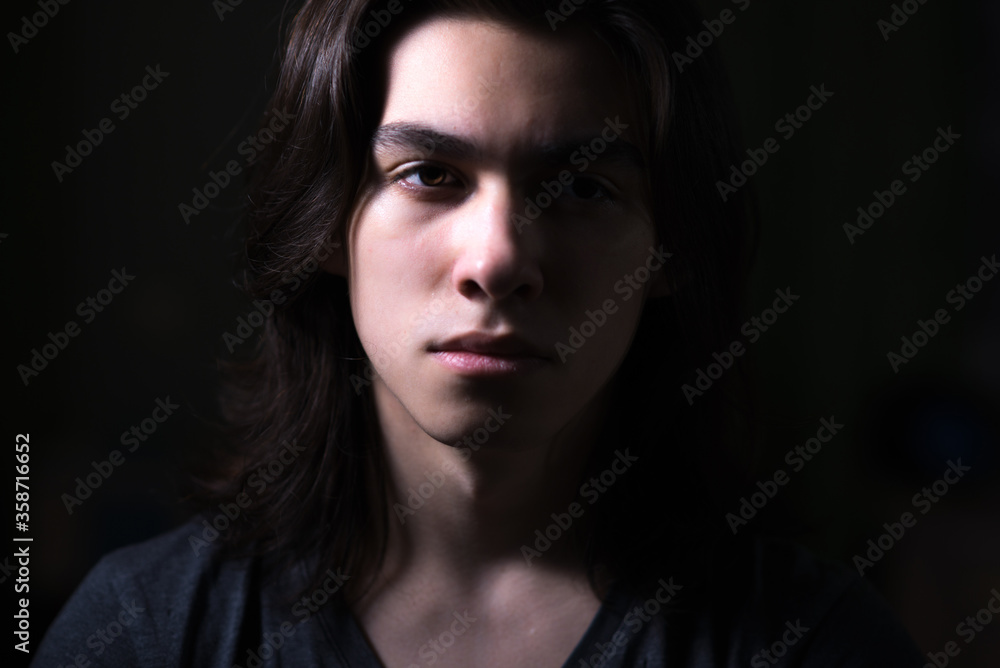 Portrait of young man with long hair in low key with Rembrandt lightning