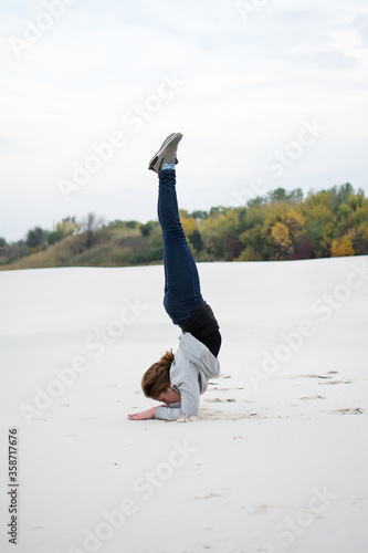 A young girl goes in for sports on the beach. Acrobatics. Young woman performs yoga exercises 