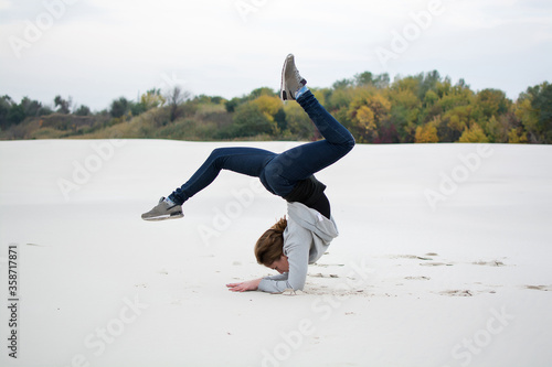 A young girl goes in for sports on the beach. Acrobatics. Young woman performs yoga exercises 