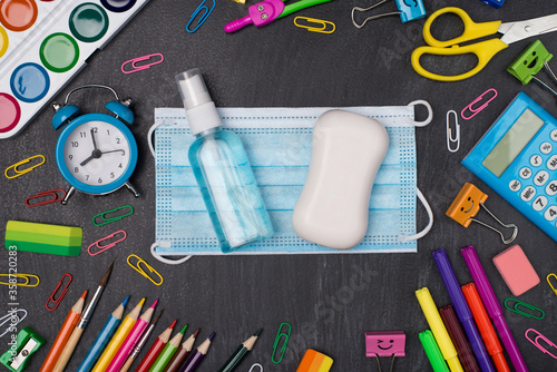 Staying healthy and educated concept. Top above overhead view photo of colorful stationery with mask soap and hand sanitizer in center isolated on blackboard