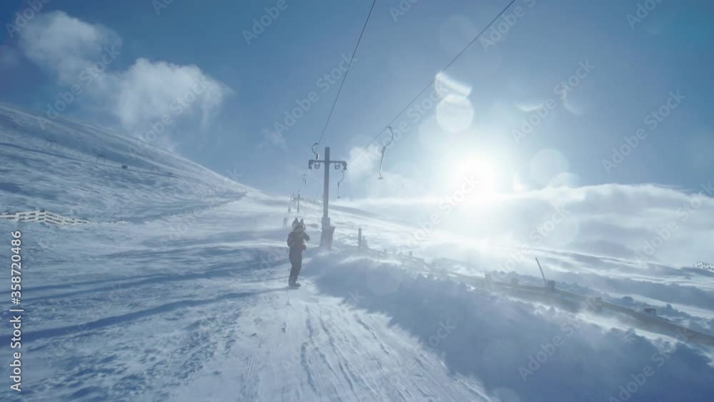 Following shot of snowboarder riding button lift with high winds and spindrift blowing across and into the lens. Nevis Range Scotland. Following shot of snowboarder riding button lift with high winds and spindrift blowing across and into the lens. Nevis Range Scotland.