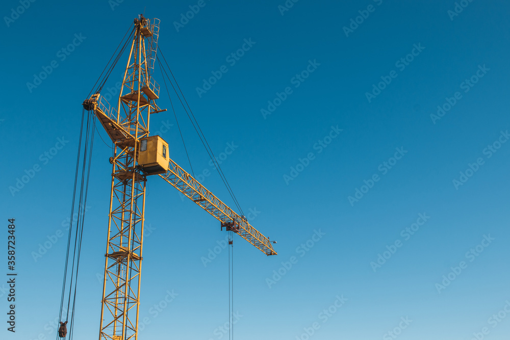 Top of a yellow construction hoisting crane against a blue sky background.