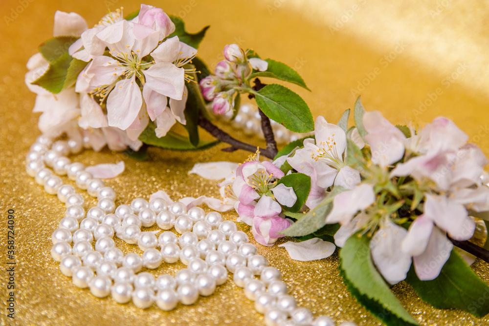Pearl necklace and Apple blossom branch on a Golden background
Pearl necklace and Apple blossom branch on a Golden background