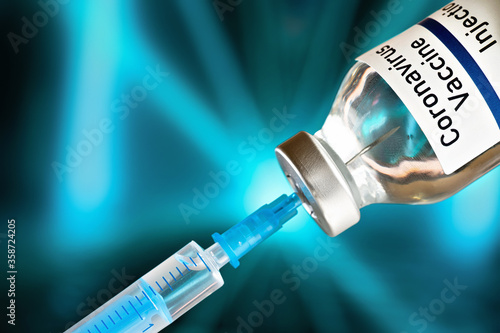 Coronavirus covid-19 vaccine concept -  glass bottle with silver cap hypodermic syringe needle injected, vibrant color blurred background (sticker is own design - not real product)