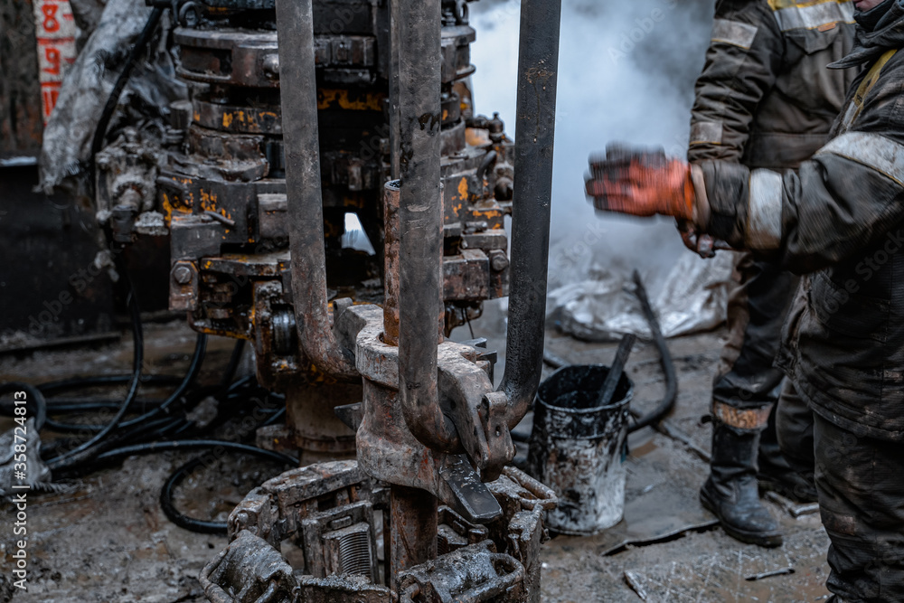 Two working drillers in a uniform, in a helmet and goggles, install drill pipes after lifting them from an oil well after drilling. The concept of a working person. Two working drillers in a uniform, in a helmet and goggles, install drill pipes after lifting them from an oil well after drilling. The concept of a working person.