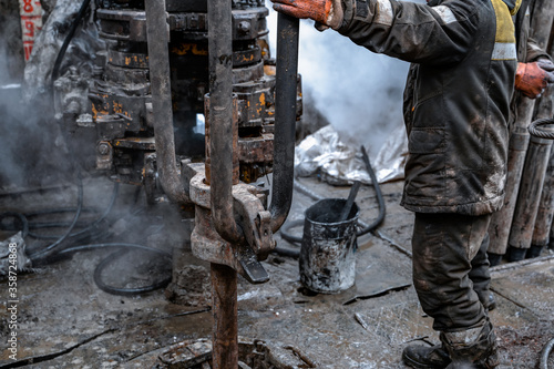 Two working drillers in a uniform, in a helmet and goggles, install drill pipes after lifting them from an oil well after drilling. The concept of a working person.