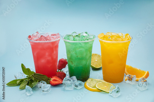 colored lemonades in plastic cups with ice, fruits and berries on a blue background
