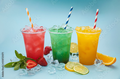 colored lemonades in plastic cups with ice, fruits and berries on a blue background
