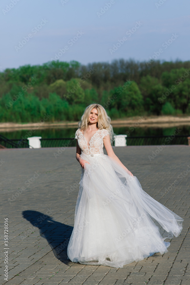 Minsk, Belarus - 05.05.2020. Young attractive blonde bride with curly hair walking in the park and smiling