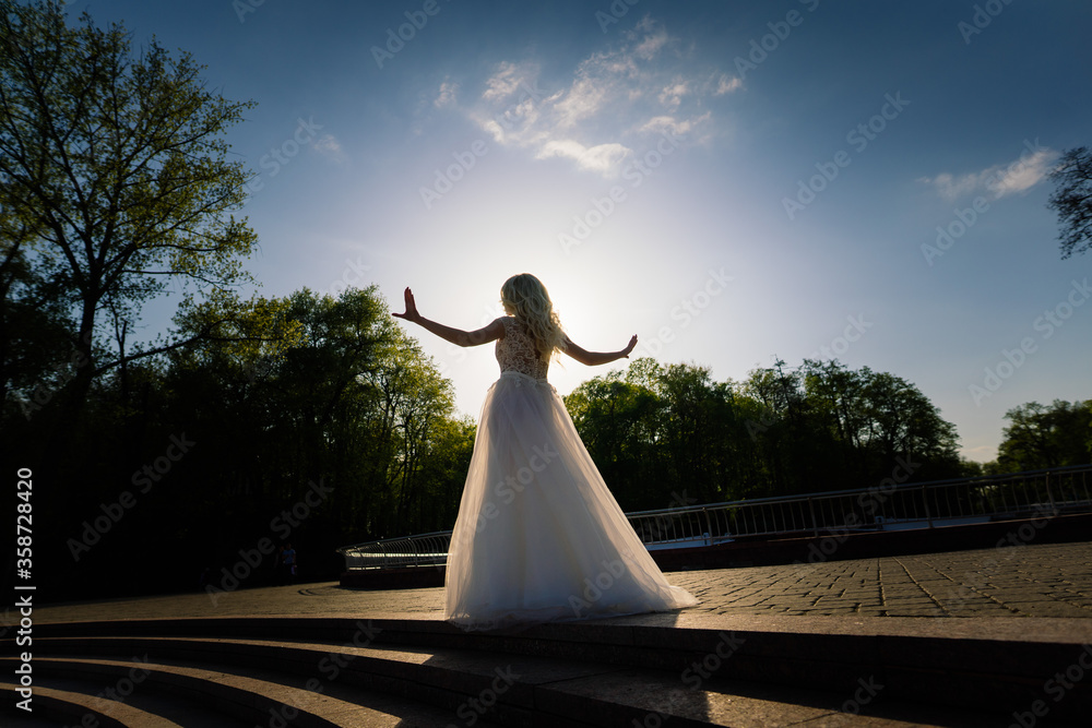 Minsk, Belarus - 05.05.2020. Young attractive blonde bride with curly hair walking in the park and smiling Minsk, Belarus - 05.05.2020. Young attractive blonde bride with curly hair walking in the park and smiling