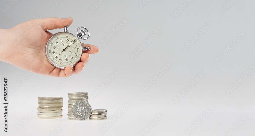 time is money. hand holding a stopwatch on a stack of silver coins ...