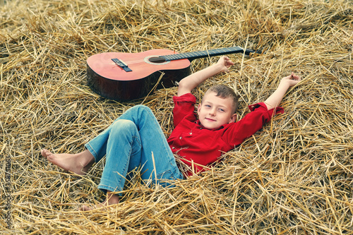Portrait of a boy with an acoustic guitar in a field near a haystack