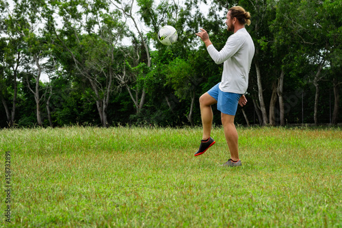 young attractive man training with soccer ball on soccer green field background