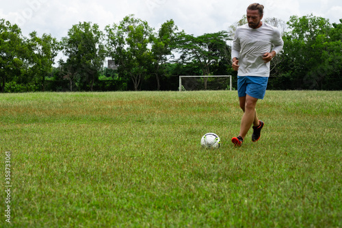 young attractive man training with soccer ball on soccer green field background