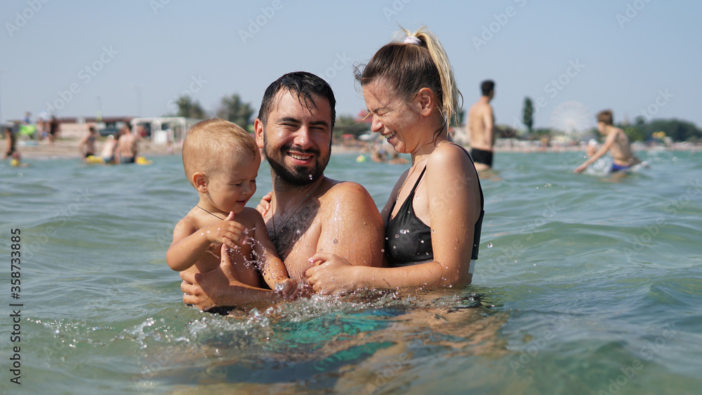 Young family standing in water in sea. Father holding little son in arms Young family standing in water in sea. Father holding little son in arms