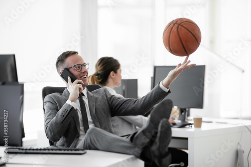 Businessman talking to the phone. Handsome businessman with basketball in office. 