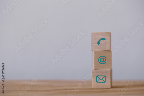 Three wood cube block stacking with contact Icon arranging In a row on wood background. Concept of business strategy and action plan.