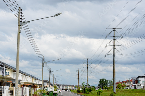 Kuching, Sarawak / Malaysia - June 21, 2016: Power poles and cables alongside street lighting in residential housing area in overcast sky.