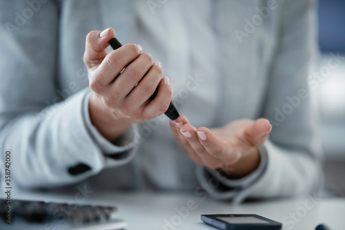 Close up of businesswoman using lancet pen in office. Young woman checking blood sugar level	