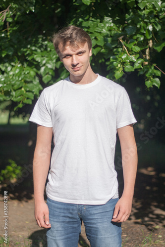 a happy young man stands in the sun in a white t shirt with a smile on his face