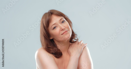 Sexy mature woman with naked shoulders looks at camera touching shoulder with hand. Body care concept. Blank for ad banner.